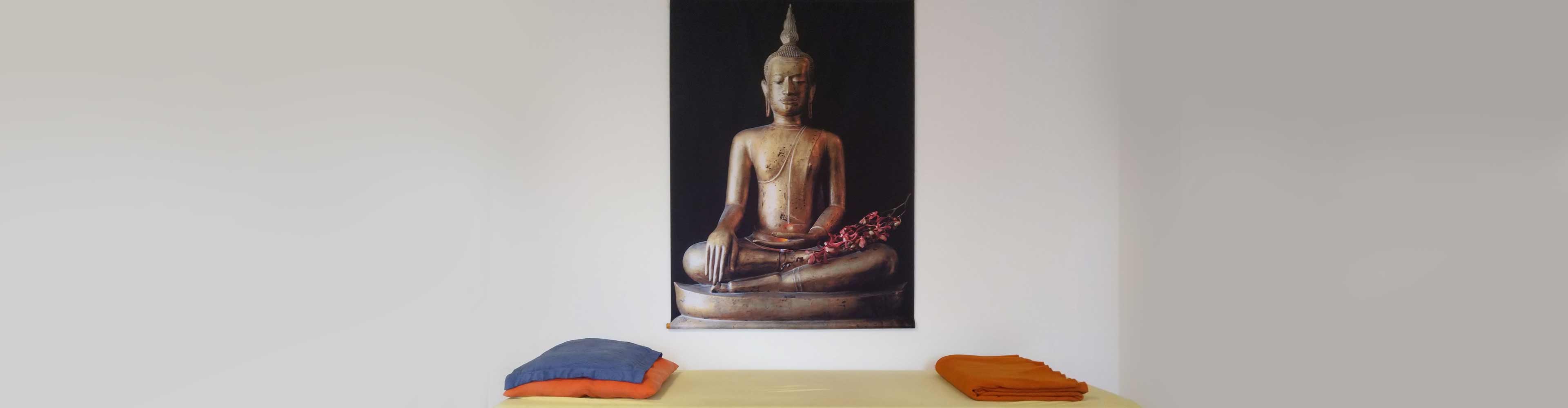 Ein Budda-Bild über einer Behandlungslige mit Kissen und zusammengelegter Decke.